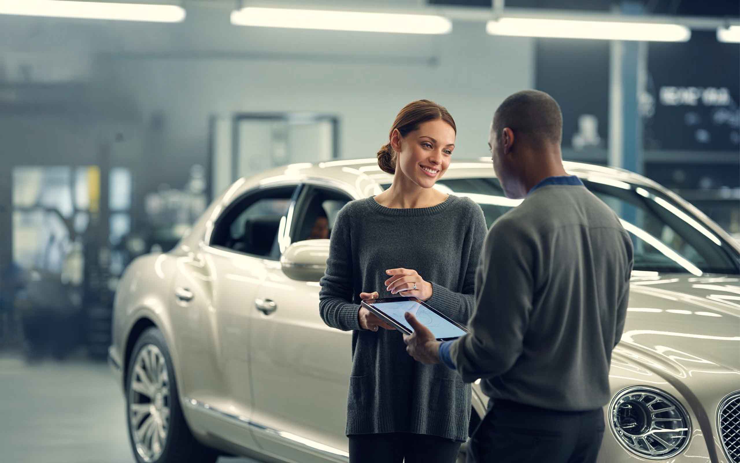 Employee with tablet speaking to smiling customer in front of bentley sedan - craigs collision