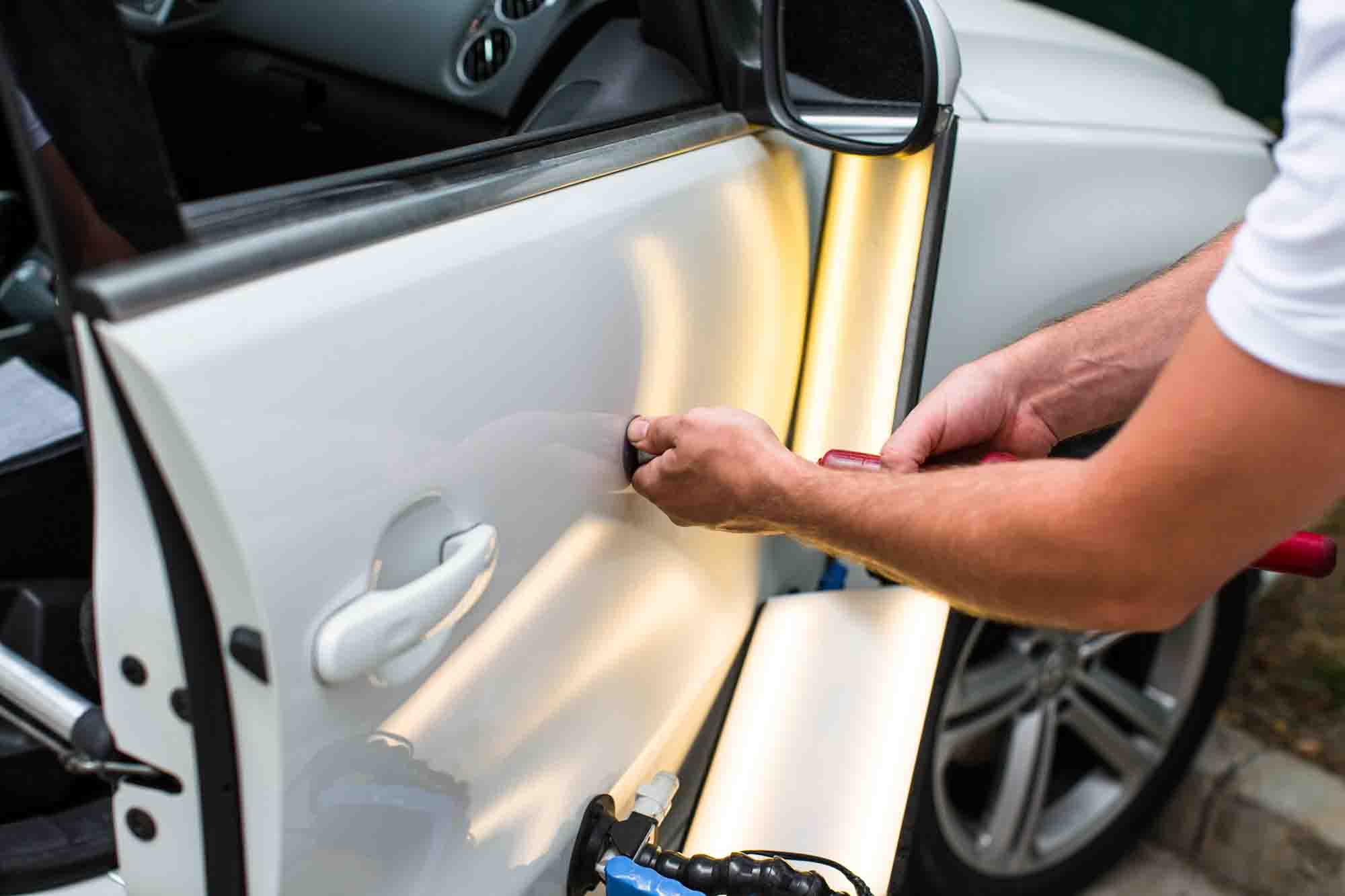 Technician performing paintless dent repair on passenger door of white sedan - auto body shop - collision repair services - craigs collision